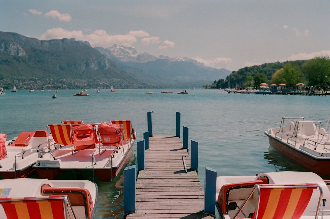home-hero-1 Explore the tranquil beauty of Lake Annecy with docked pedal boats and stunning mountain views.
